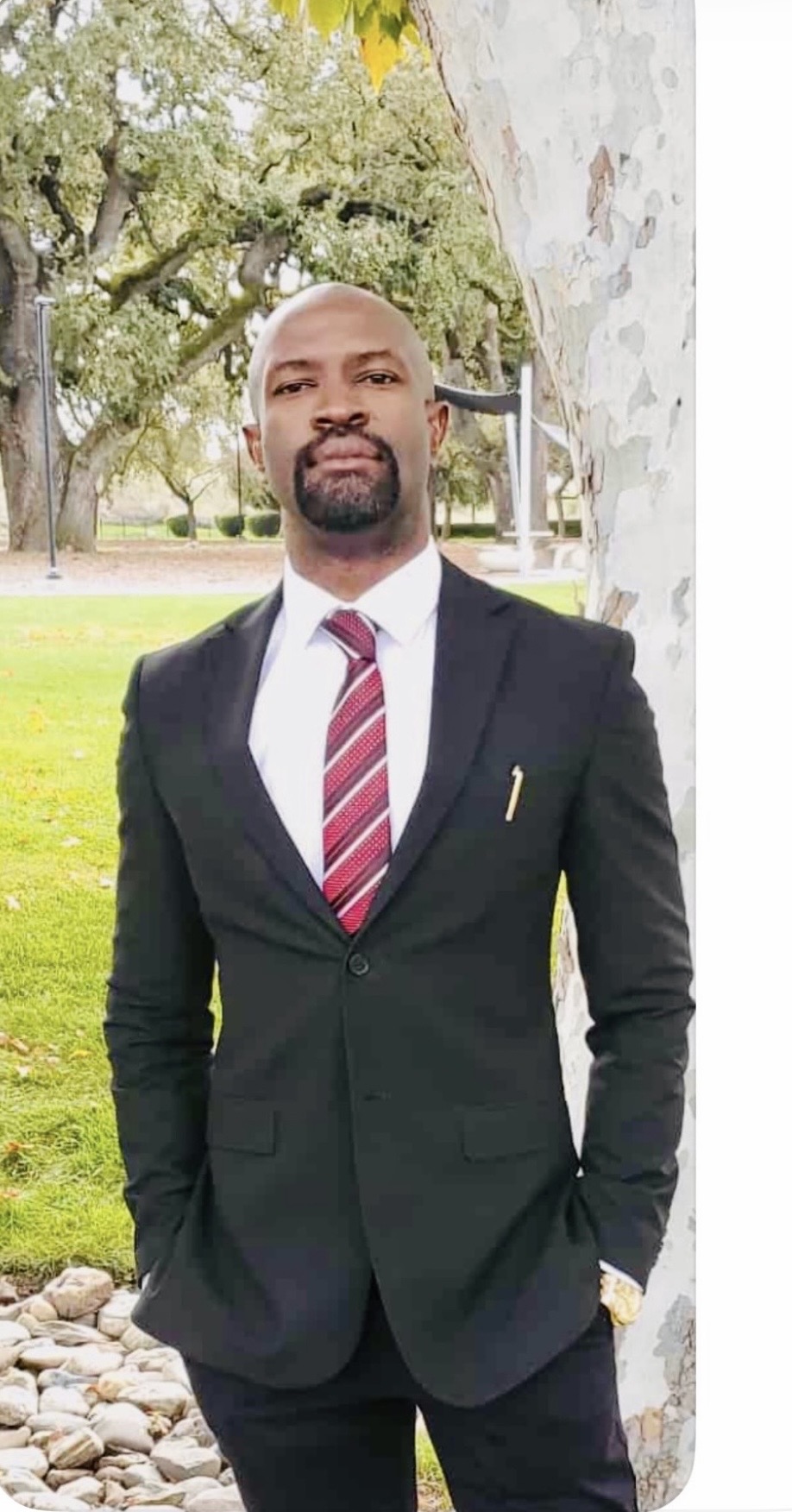 Ralph Nwobi in a black suit by a stone wall