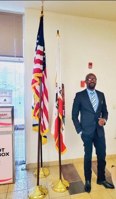 Ralph Nwobi standing with American and California flags
